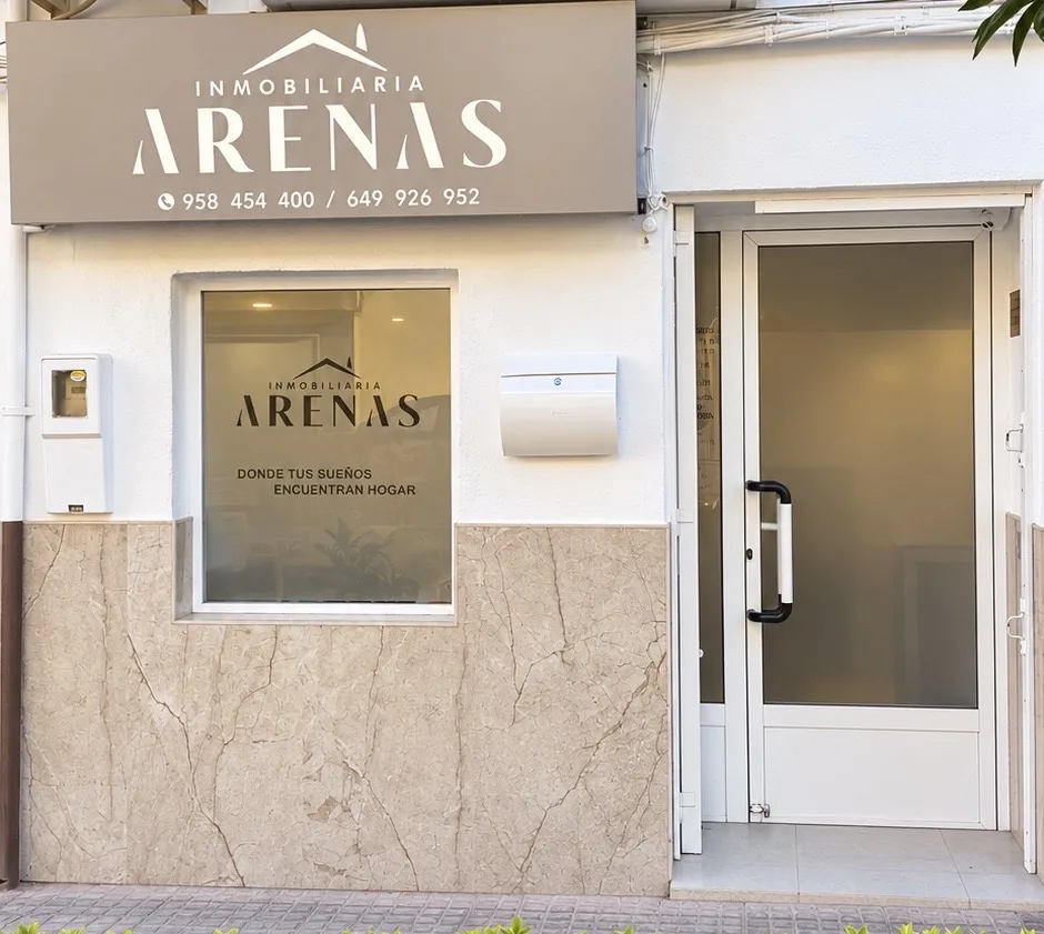 Fachada de la oficina de Inmobiliaria Arenas en la calle Real de Valderrubio, con el rótulo, la ventana y la puerta de entrada
